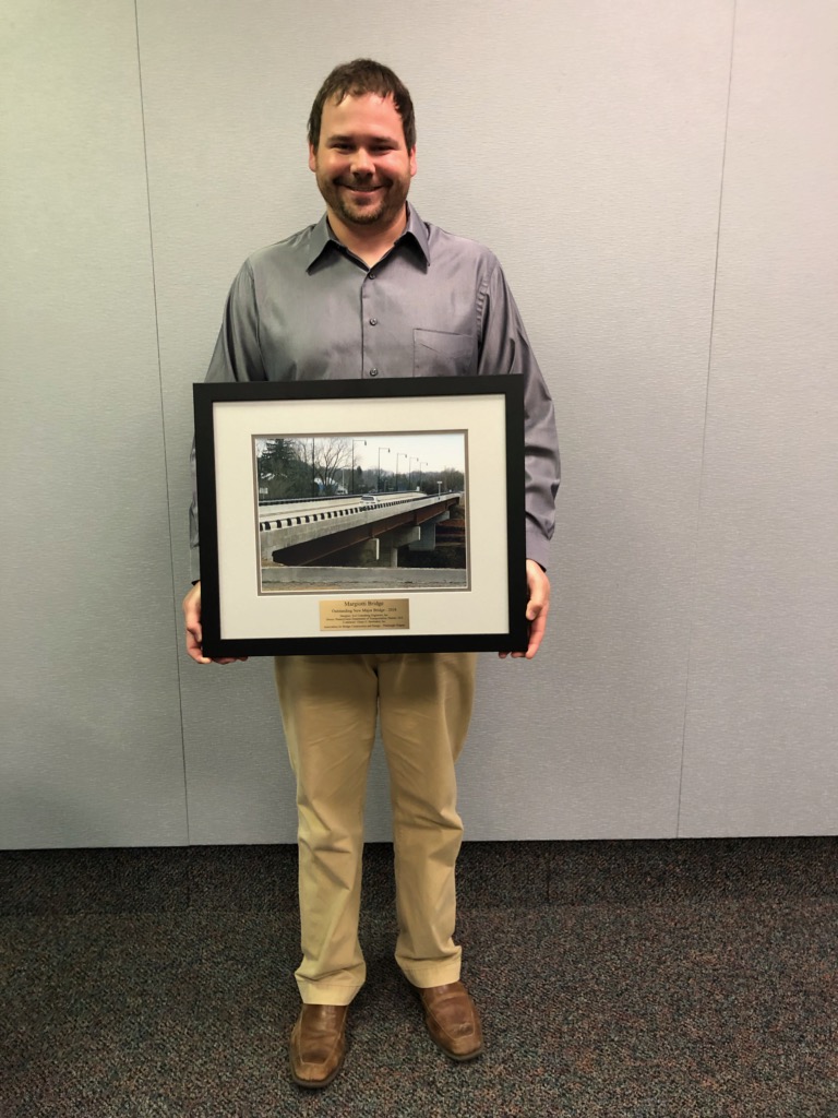 Jason Layman stands holding a large framed picture of the Margiotti Bridge.