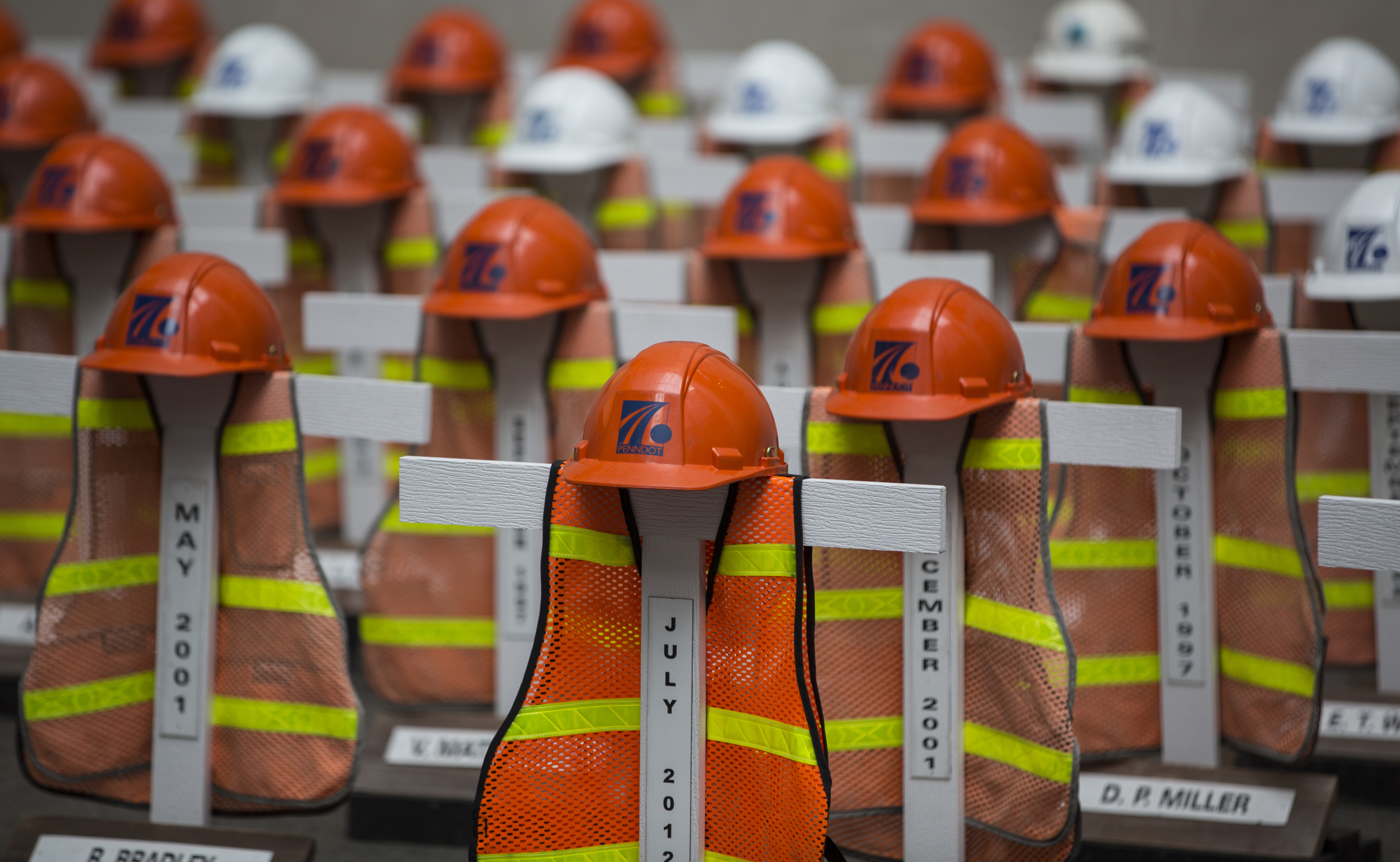 display of white crosses each draped with an orange safety vest and construction helmet