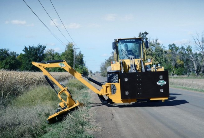 Heavy equipment using a brushing loader attachment to mow grass and clear brush on the side of a road.