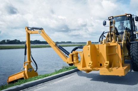 Heavy equipment using a brushing loader attachment to mow grass and clear brush along a road.
