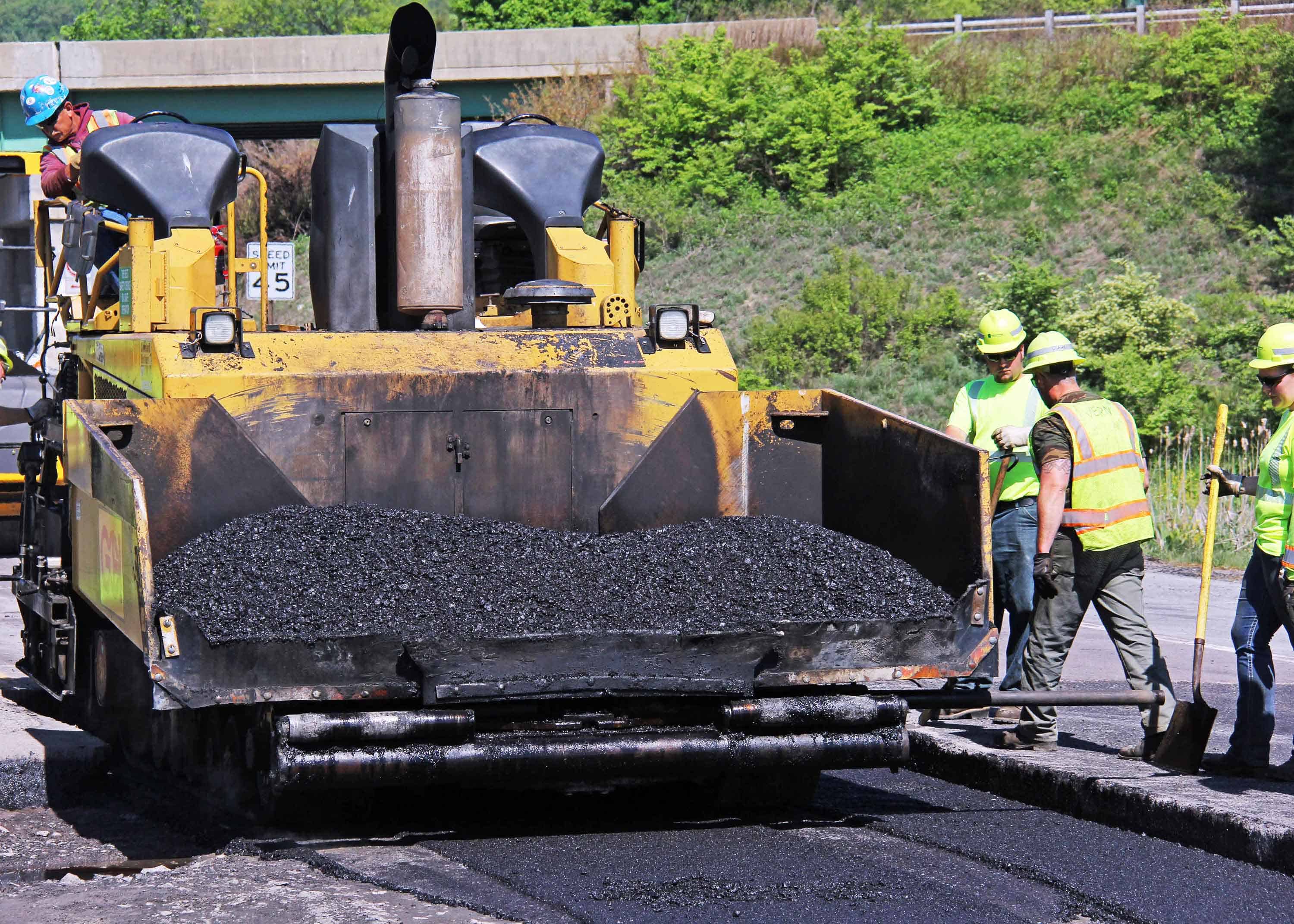 A construction vehicle pours warm mix asphalt on a roadway.