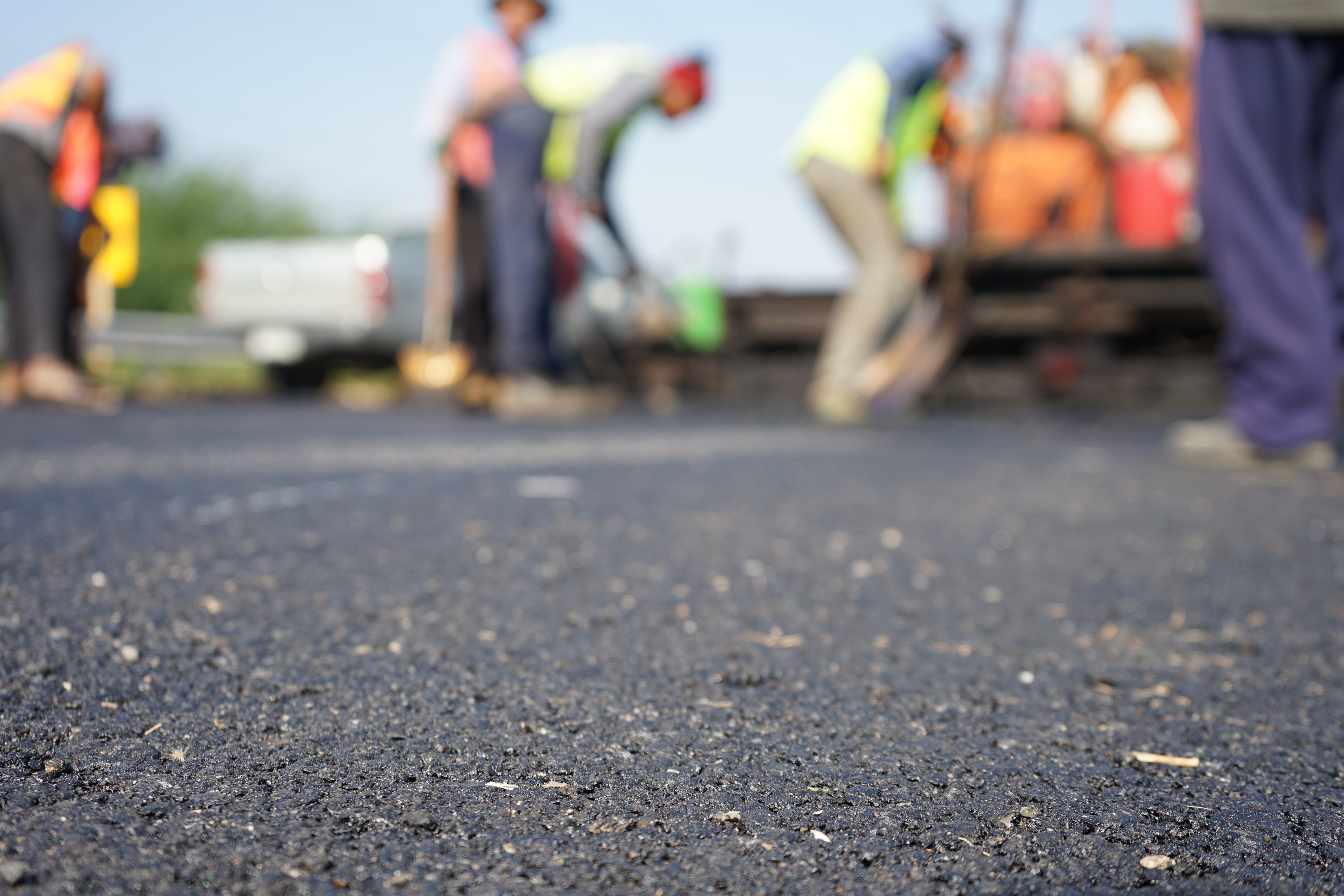 Out-of-focus construction workers working on a paved roadway.