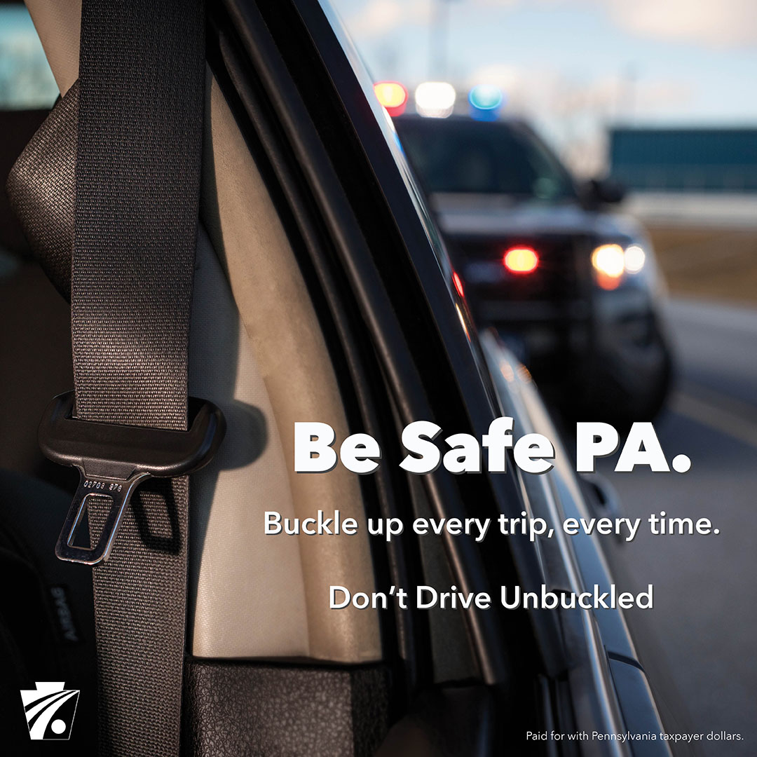 Image of unbuckled seat belt with police car in the background with text reading Be Safe PA. Buckle up every trip, every time.Don't Drive Unbuckled.